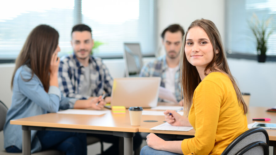 portrait of young woman in casual wear working in creative business startup company office with coworker people in background portrait of young woman in casual wear working in creative business startup company office with coworker people in background