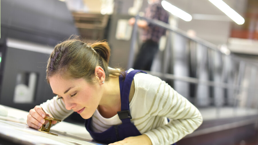 Woman in printing house using magnifying glass